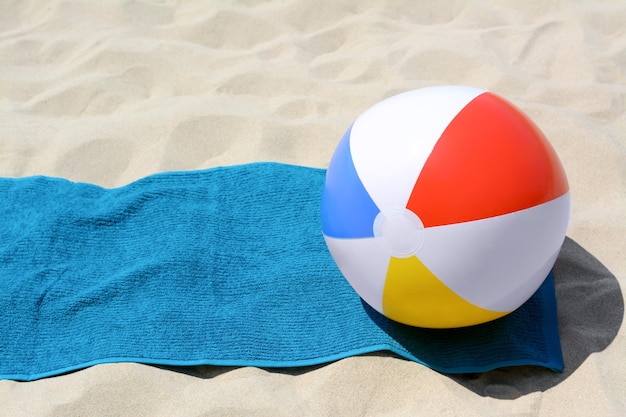 Blaues Handtuch und bunter Wasserball auf Sand