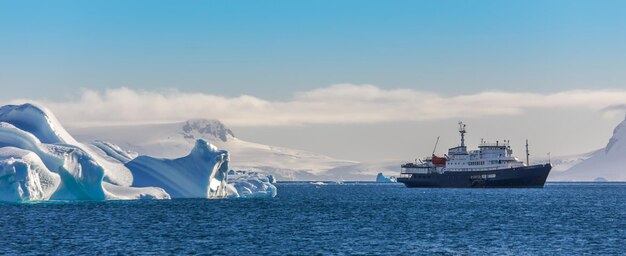 Blaues Kreuzfahrtschiff zwischen den Eisbergen mit Gletscher im Hintergrund Südliche Shetlandinseln Antarktis