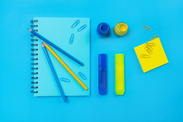 Blaues Notizbuch mit schwarzen Ringen mit einer blauen Markierung an der Spitze mit einer Handvoll Büroklammern und Bleistiften in Blau und Blau und einer Flasche Farbe. A von Büromaterial. Gelb und blau.