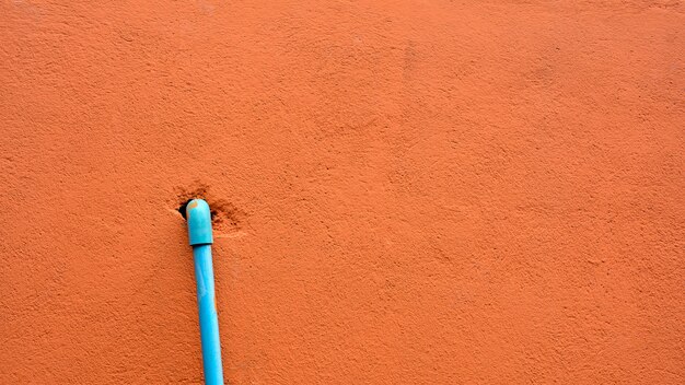 Blaues Plastikrohr an der orange Zementwand.