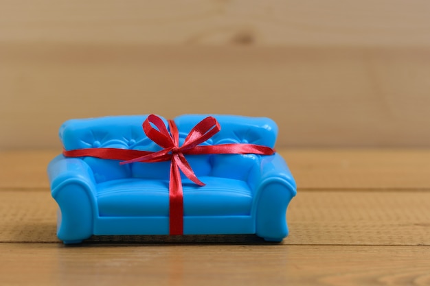 Blaues Sofa gebunden mit einem roten Geschenkband auf dem hölzernen Hintergrund. Ungewöhnliches Geschenk.