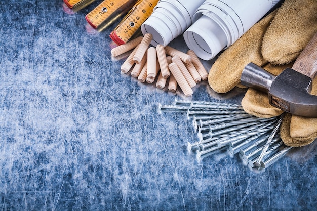 Blaupausen hämmern Schutzhandschuhe aus Holz, Meterkonstruktionsnägel und Dübelhaufen auf zerkratztem Wartungskonzept für metallische Oberflächen