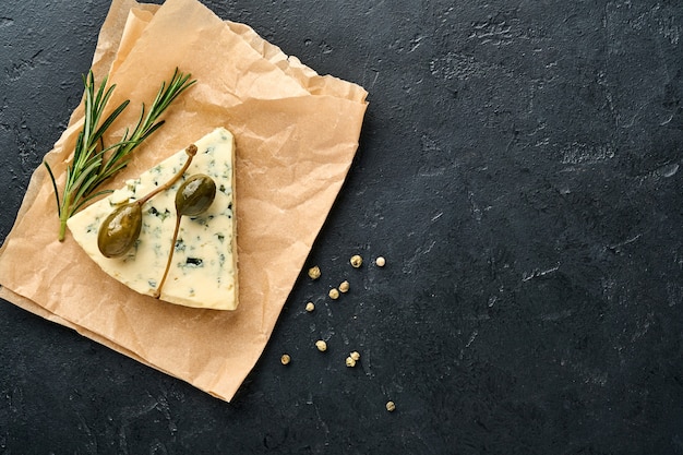 Blauschimmel- oder Briekäsestücke auf Pergamentpapier mit Honig, Rosmarin, Kapern und Pfeffer