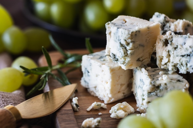 Blauschimmelkäse mit einem Käsemesser auf einem Holzbrett vor dem Hintergrund von Trauben