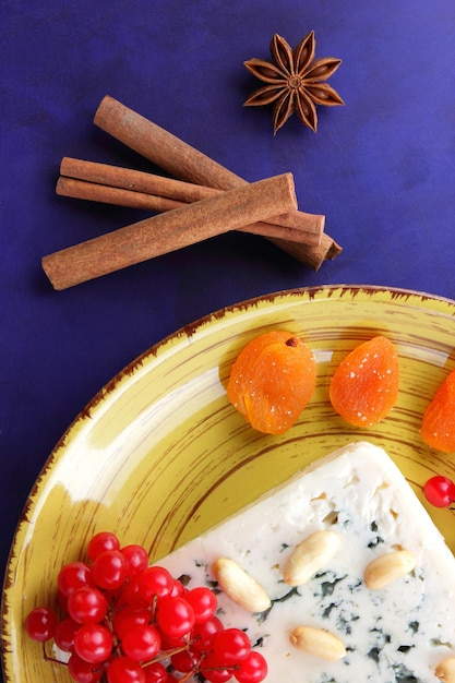 Blauschimmelkäse mit Nüssen, Beeren und getrockneten Früchten auf einem gelben Teller Käse auf blauem Hintergrund Detailansicht Ansicht von oben