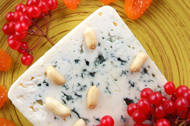 Blauschimmelkäse mit Nüssen, Beeren und getrockneten Früchten auf einem gelben Teller Käse auf blauem Hintergrund Detailansicht Ansicht von oben