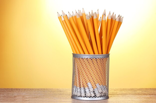 Bleistifte in Metallbecher auf Holztisch auf gelbem Hintergrund