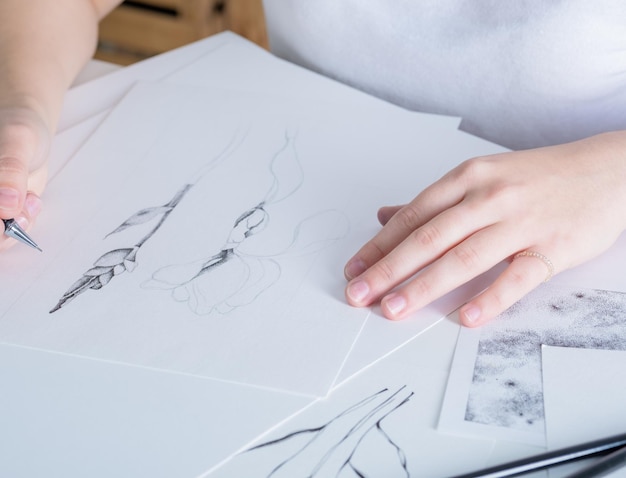 Bleistiftzeichnungen liegen auf dem Tisch Eine junge Frau mit europäischem Aussehen zeichnet mit einem Bleistift auf weißem Papier Grafiken Der Prozess des Zeichnens mit einem Bleistift zu Hause an einem weißen Tisch