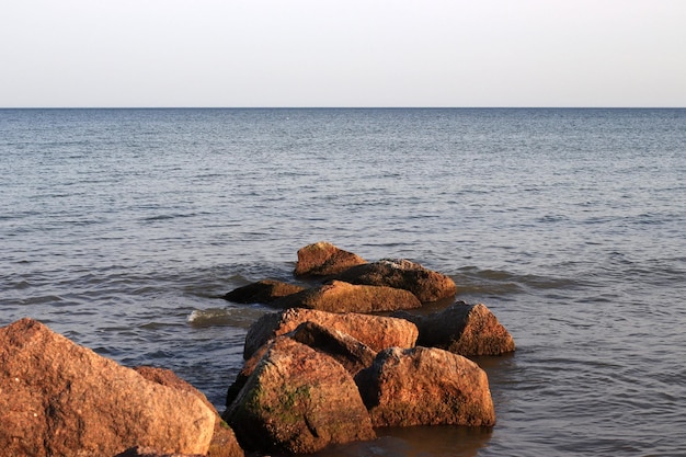 Blick auf das blaue Meer bis zum Horizont im Vordergrund große Steine im Wasser