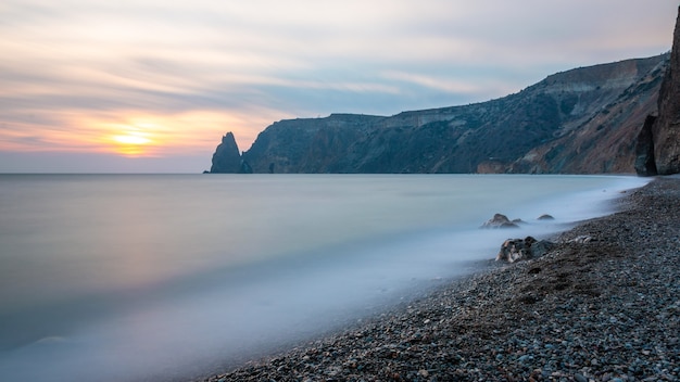 Blick auf das Sonnenuntergangsmeer und den Strand, der Felsenvulkangestein wird durch den warmen Sonnenuntergang, Sand und Kieselsteine, vulkanischen Basalt wie in Island beleuchtet.