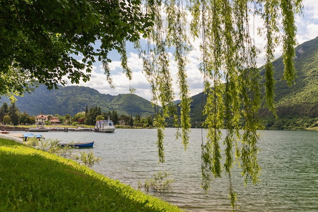 Blick auf den alpinen Lago d'Idro, eingerahmt von langen grünen Weidenzweigen, Bootssteg, Brescia, Lombardei, Italien