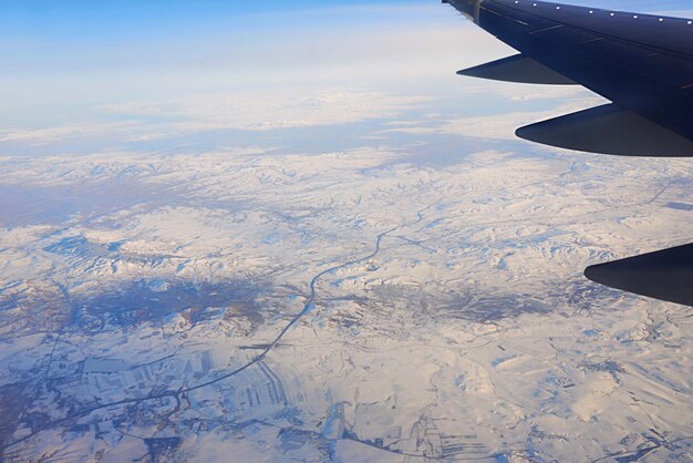 Blick auf den Flügel des Flugzeugs in den Himmel und die schneebedeckten Berge