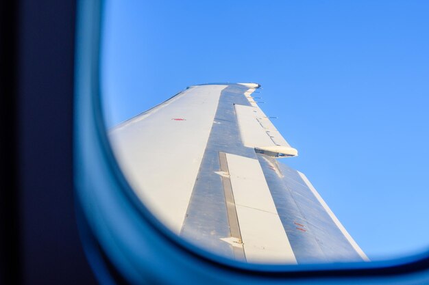 Blick auf den Flugzeugflügel gegen den blauen Himmel durch das Fenster