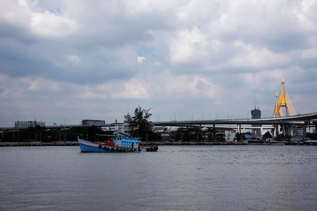 Blick auf den Landschaftswolkenhimmel und das Stadtbild von Samutprakarn mit Lastkahn und Schlepper-Frachtschiff-Lieferversand im Chao Phraya-Fluss im Bezirk Phra Pradaeng und Bhumibol-Brücke in Samut Prakan Thailand