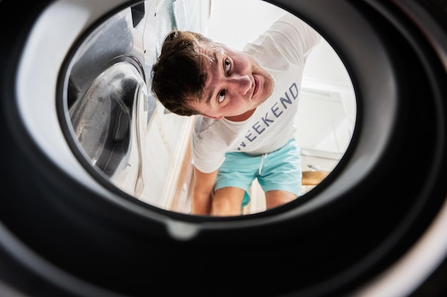 Blick auf den Mann von der Waschmaschine im Inneren Männlich wäscht die tägliche Routine