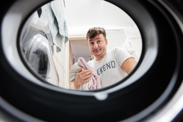 Blick auf den Mann von der Waschmaschine im Inneren Männlich wäscht die tägliche Routine