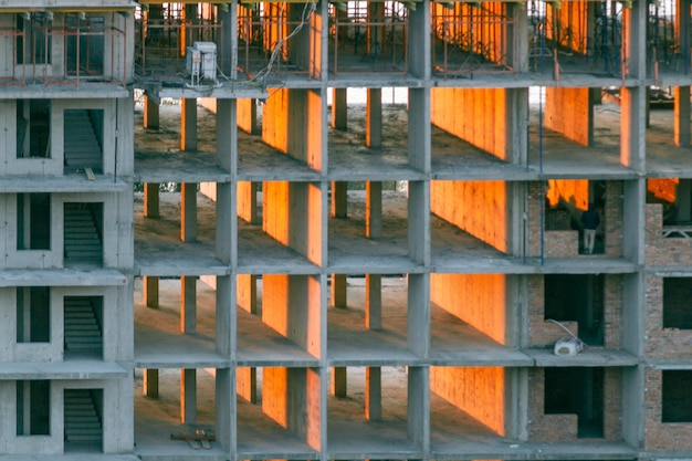 Blick auf den Rahmen eines mehrstöckigen Wohngebäudes mit Hochhauskranen, die von den Strahlen der untergehenden Sonne beleuchtet werden Sonnenstrahlen, die durch den Rahmen eines im Bau befindlichen Gebäudes gehen