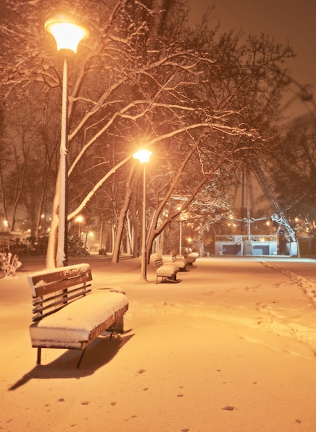 Blick auf die Bank gegen den Weihnachtsbaum und die leuchtende Laterne durch Schneien