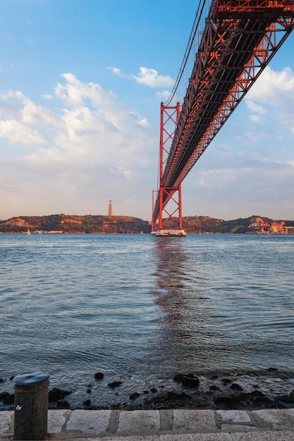 Blick auf die Brücke 25 de Abril über den Fluss Tejo, das Christus-König-Denkmal und einen Kai in Lissabon, Portugal