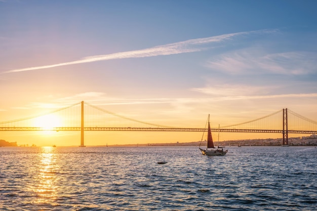 Blick auf die Brücke 25 de Abril von Lissabon mit Yachtsilhouette bei Sonnenuntergang Lissabon Portugal