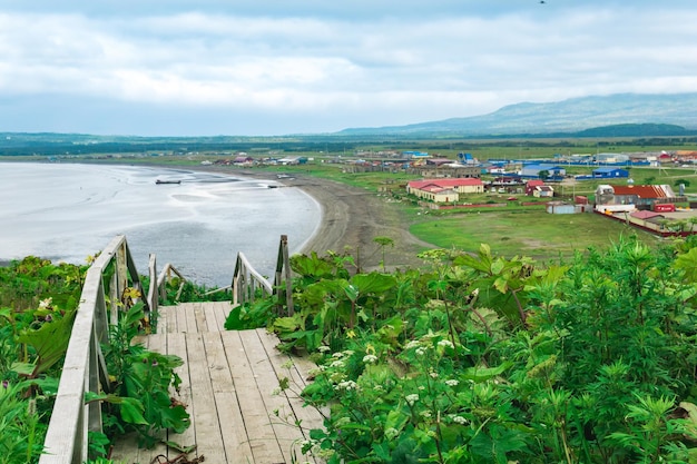 Blick auf die Bucht von YuzhnoKurilsk auf der Insel Kunaschir von einem hohen Kap im Vordergrund ein hölzerner Bürgersteig mit einer Leiter