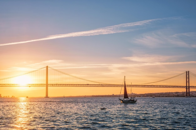 Blick auf die de abril-brücke über den fluss tejo bei sonnenuntergang in lissabon, portugal