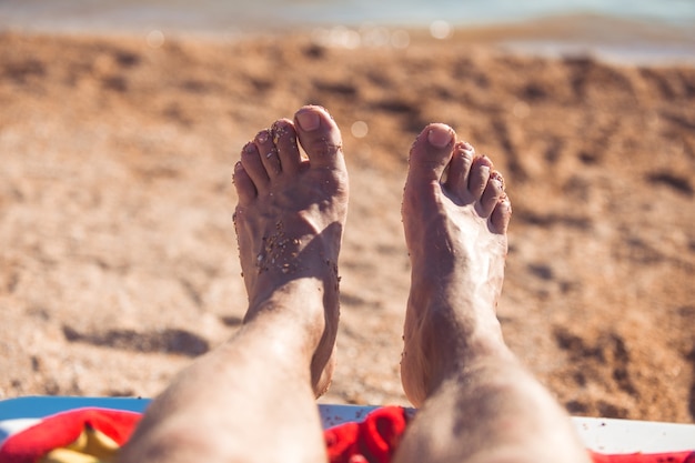 Blick auf die Füße des Menschen, die am Strand mit Sand bedeckt sind.