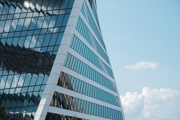 Blick auf die Glasfassade eines Wolkenkratzers und den blauen Himmel mit weißen Wolken. Moderne Architektur im städtischen Raum. Abstrakter Hintergrund