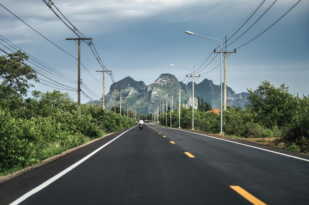 Blick auf die grüne Bergkette mit Strommast und Laternenpfahl auf der Autobahn in der Landschaft bei Sam Roi Yot, Prachuap Khiri Khan