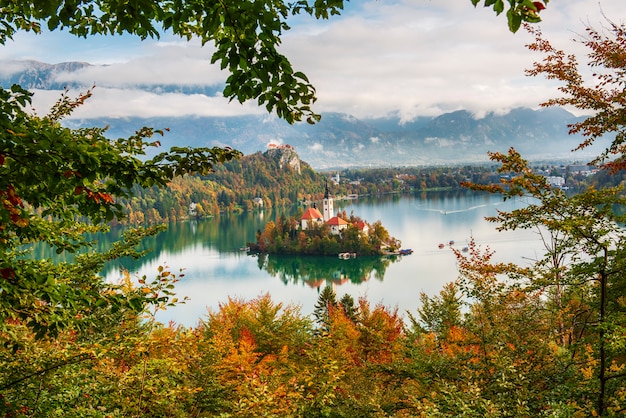 Blick auf die Kirche Mariä Himmelfahrt im Bleder See, Slowenien im Herbst mit bunten Bäumen