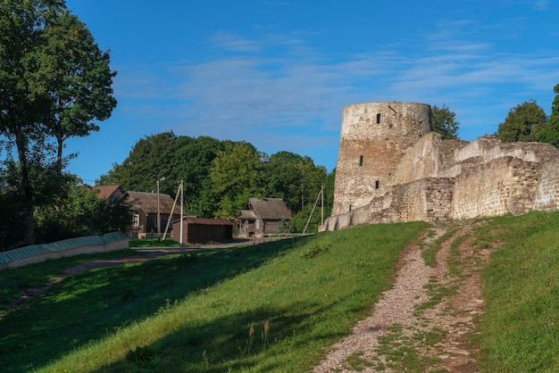 Blick auf die Mauer und den Turm der Festung Izborsk vor dem Hintergrund eines Dorfes an einem sonnigen Sommertag Region Izborsk Pskow Russland