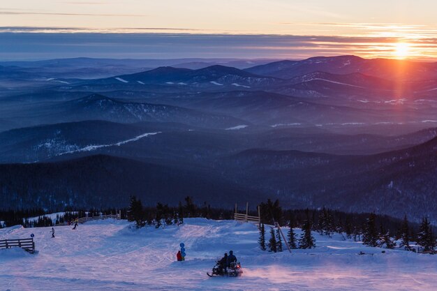 Blick auf die Piste des Skigebiets bei Sonnenuntergang mit einem Schneemobil