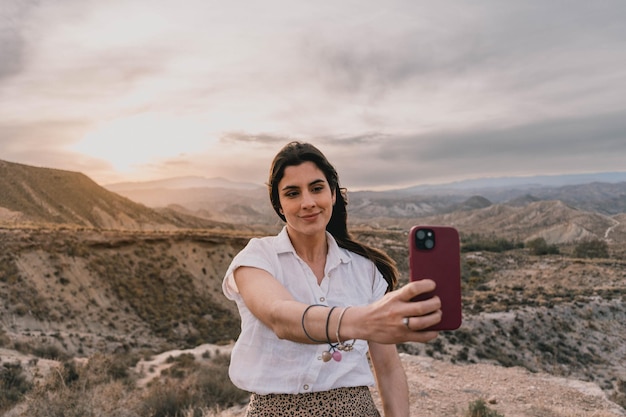 Blick auf eine Frau, die bei Sonnenuntergang ein Selfie mit ihrem Mobiltelefon macht, mit der Wüste im Hintergrund