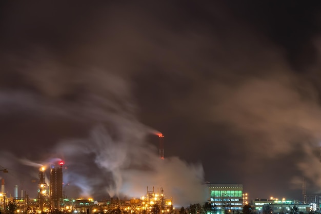 Blick auf eine große Fabrik oder Anlage im Licht der Nachtbeleuchtung Viel Rauch kommt aus den Schornsteinen der Fabrik Ein Unfall in einer Ölraffinerie Ein Feuer auf dem Gelände der Fabrik