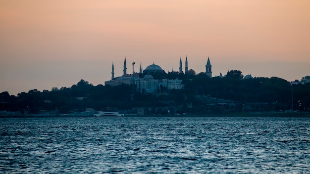 Blick auf eine Moschee und viel Grün um sie herum am Abend, Bosporus-Straße im Vordergrund in Istanbul, Türkei