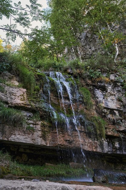 Blick auf einen kleinen Gebirgsflusswasserfall zwischen großen Kopfsteinpflastersteinen von einer Klippe aus