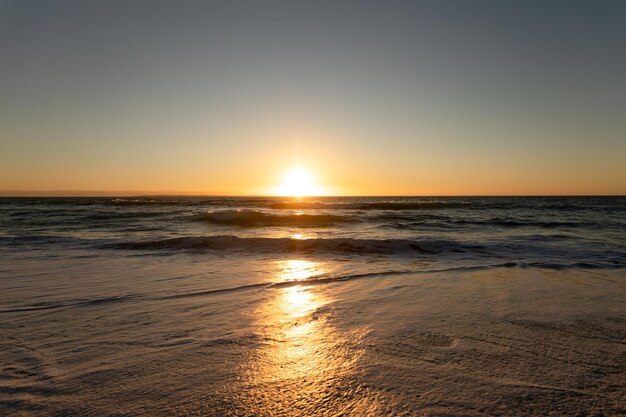 Blick auf einen Sandstrand und ein ruhiges Meer mit Wellen und blauem Himmel bei Sonnenuntergang