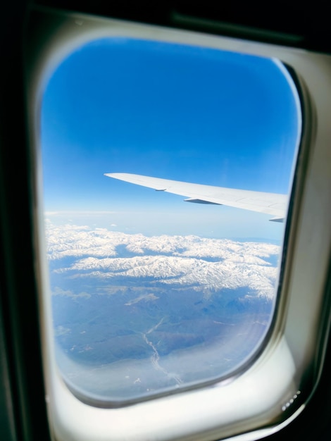Blick auf schneebedeckte Gipfel und blauen Himmel aus dem Flugzeugfenster
