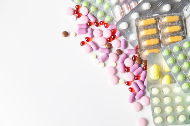 Blick auf verstreute Pillen und Tabletten in Packungen auf weißem Hintergrund. Von oben