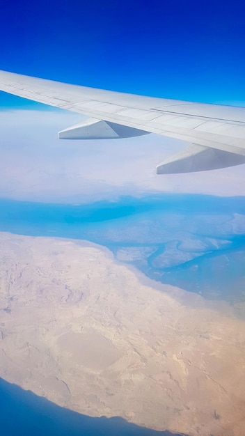 Blick aus dem Fenster des Flugzeugs auf blauen Himmel und Erde mit Landschaft aus Wüstenmeer und Kanälen