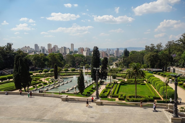 Blick aus der Vogelperspektive auf den Garten und die Brunnen des Ipiranga-Museums mit dem Stadtbild von Sao Paulo als Kulisse, Brasilien