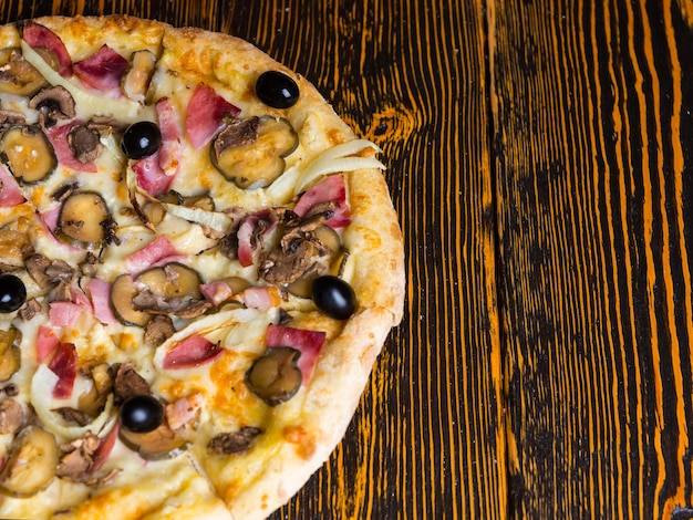 Blick aus der Vogelperspektive auf die Hälfte der leckeren Pizza mit Schinken, Pilzen, Oliven und Gurken auf Holztisch