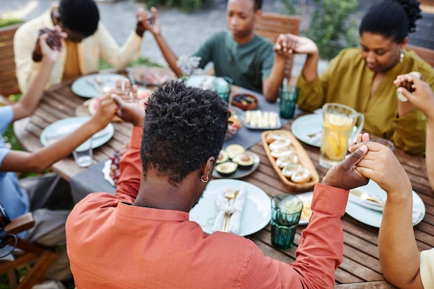 Blick aus der Vogelperspektive auf eine afroamerikanische Familie, die draußen am Tisch Anmut sagt und während g Händchen hält