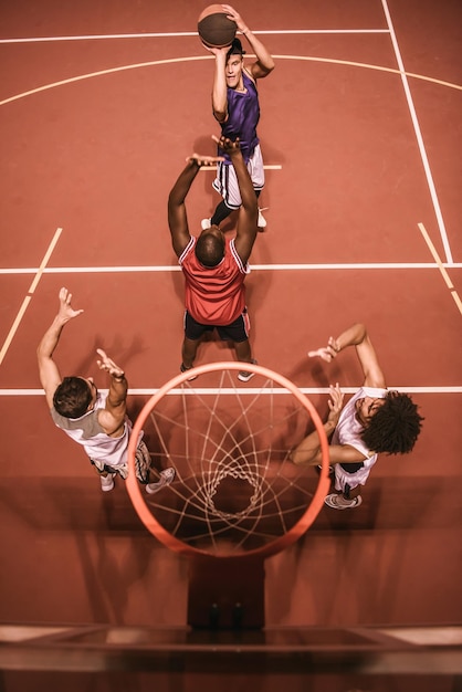 Blick aus der Vogelperspektive auf gutaussehende Jungs, die nachts im Freien Basketball spielen