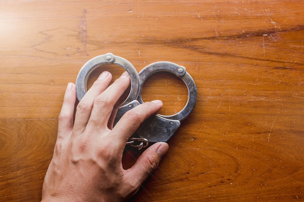 Blick direkt über der Hand, die Handschellen auf einem Holztisch hält