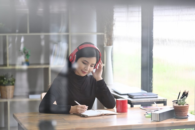 Blick durch das Fenster der hübschen Designerin, die Musik hört und in einem modernen Büro arbeitet.