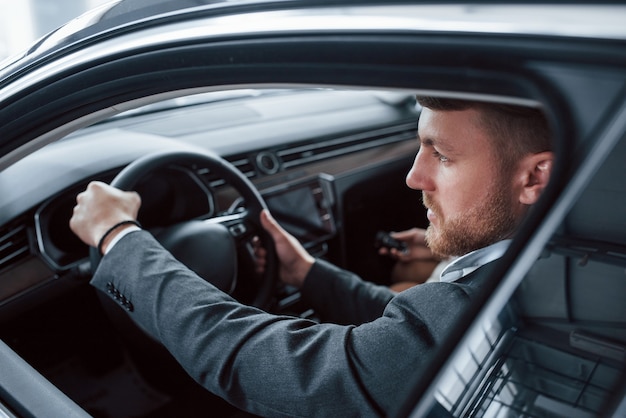 Foto blick durch das geöffnete fenster. schönes erfolgreiches paar, das ein neues auto im automobilsalon ausprobiert.