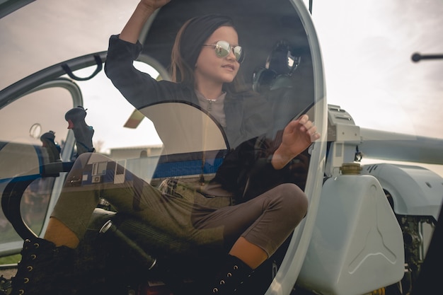 Blick durch das Glas des Hubschrauber-Cockpits des lächelnden jugendlichen Mädchens auf dem Pilotensitz
