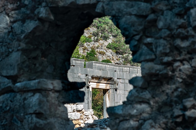 Blick durch ein Loch in der Wand auf das erhaltene Eingangsportal des antiken Tempels in den Ruinen der antiken Stadt Olympos in der Türkei