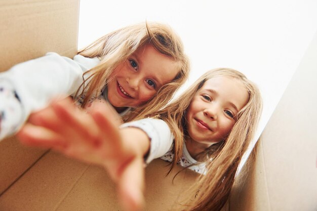 Blick in die Papierbox Zwei niedliche kleine Mädchen drinnen zu Hause zusammen Kinder, die Spaß haben